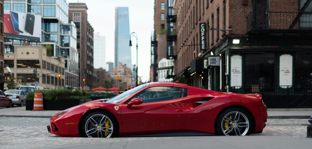 pexels-photo-2664399-2664399-1 A luxurious red Ferrari sports car parked in urban New York City against a backdrop of modern and vintage buildings.